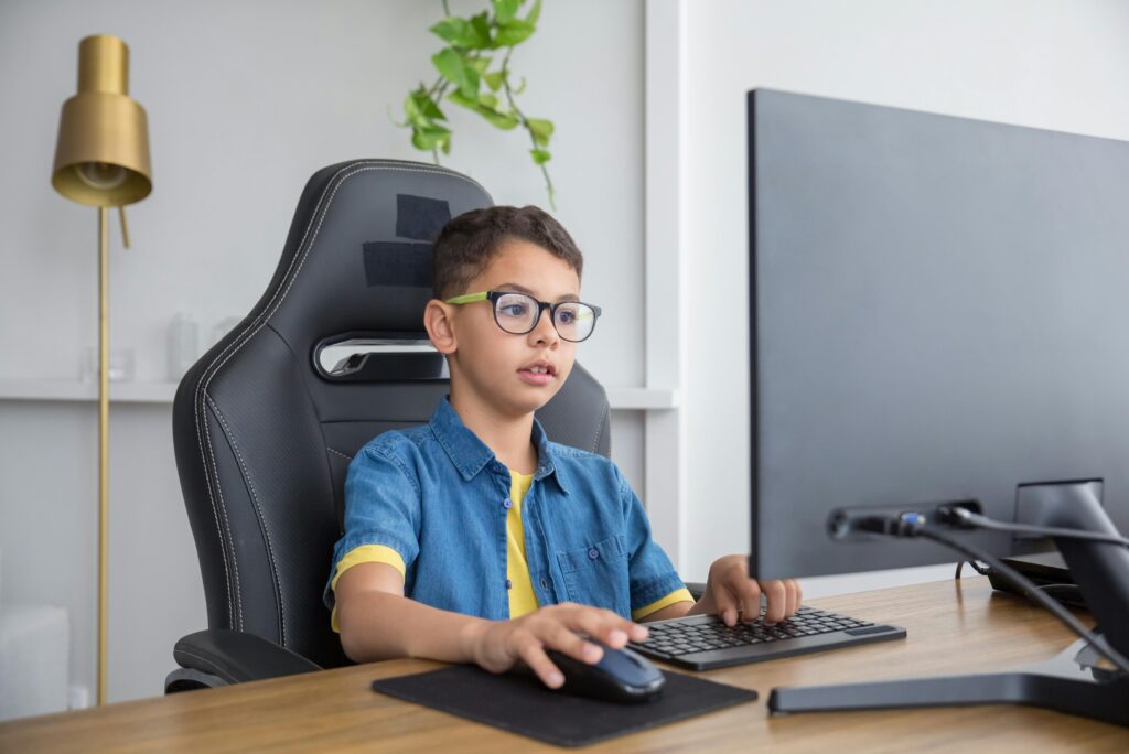 A young boy in a gaming chair focused on using a computer in a modern home office.